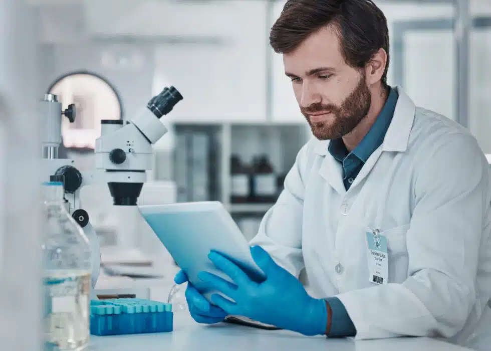 A man in a lab coat digitally tracking an OOS investigation on a tablet while next to a batch of tubes